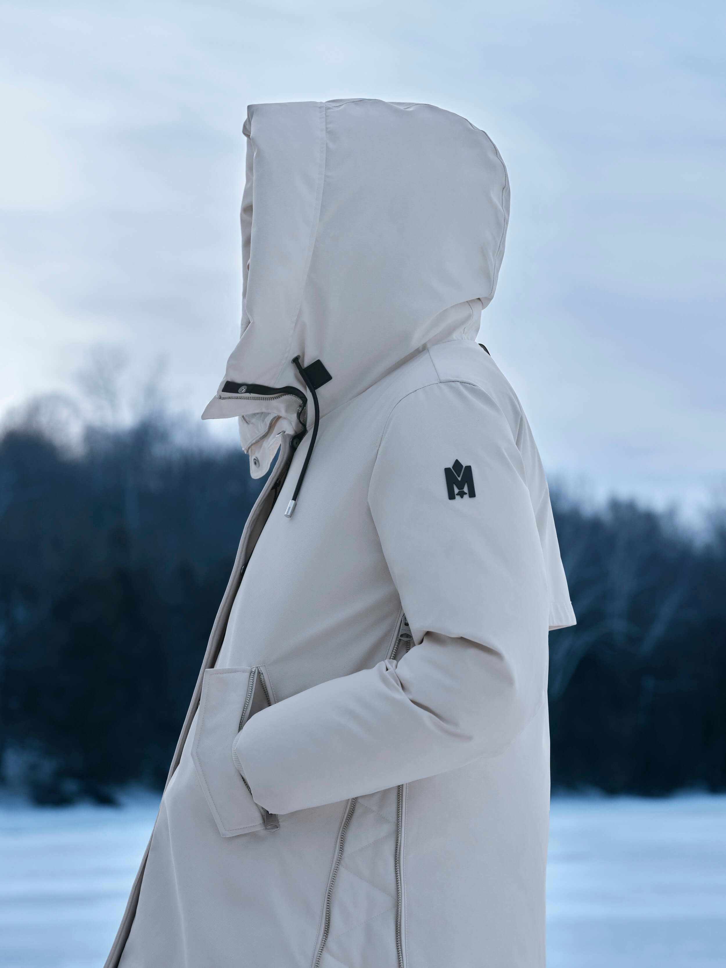 Model in Seitenaufnahme trägt weissen Mackage Mantel vor Winterlandschaft