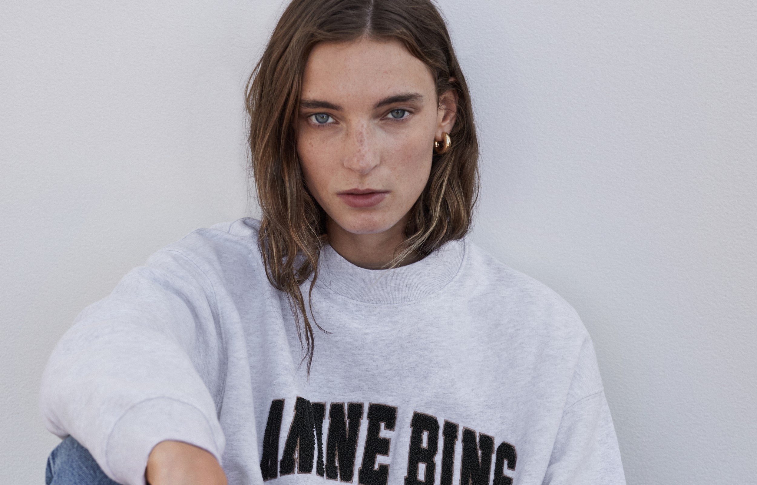 Model trägt weissen Anine Bing Pullover mit schwarzem Schriftzug Anine Bing
